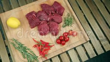 新鲜的肉做牛排在木板上。 炒肉，牛肉。 靠近西红柿，迷迭香，百里香，柠檬，红辣椒，蔓越莓..